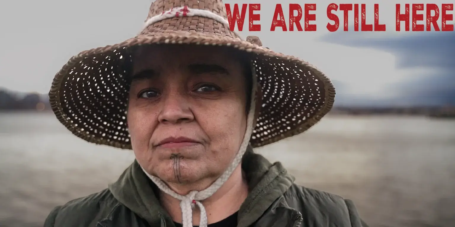 we are still here screening reception Indigenous Peoples’ Day U of A-1 woman with woven hat and green hoodie, sandy field nature background, title in red text "WE ARE STILL HERE" at the top right corner